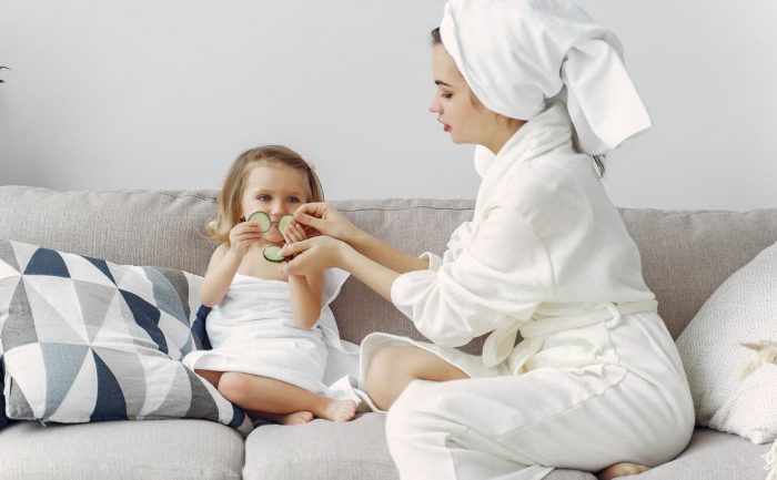 A mother and daughter enjoy a spa day at home, bonding on the couch with cucumber slices.